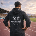 Veste coupe-vent XT noire pour running et triathlon, portée par un athlète sur piste d’athlétisme